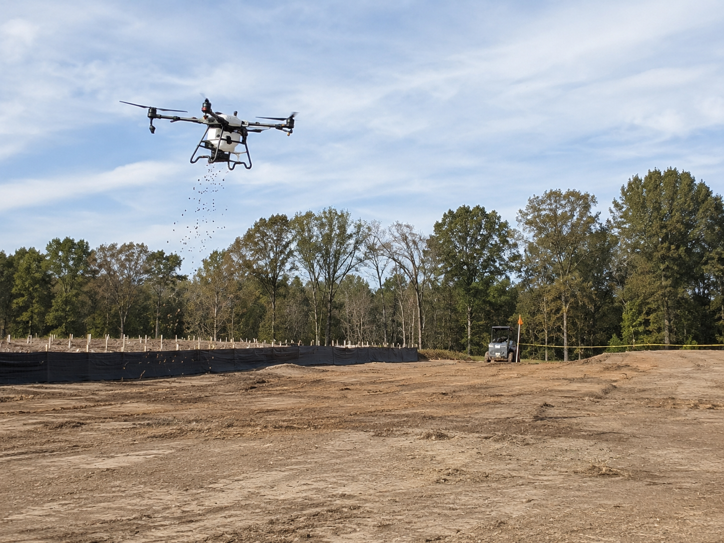 Drone seeding a cleared right-of-way with silt fence and a UTV in the background