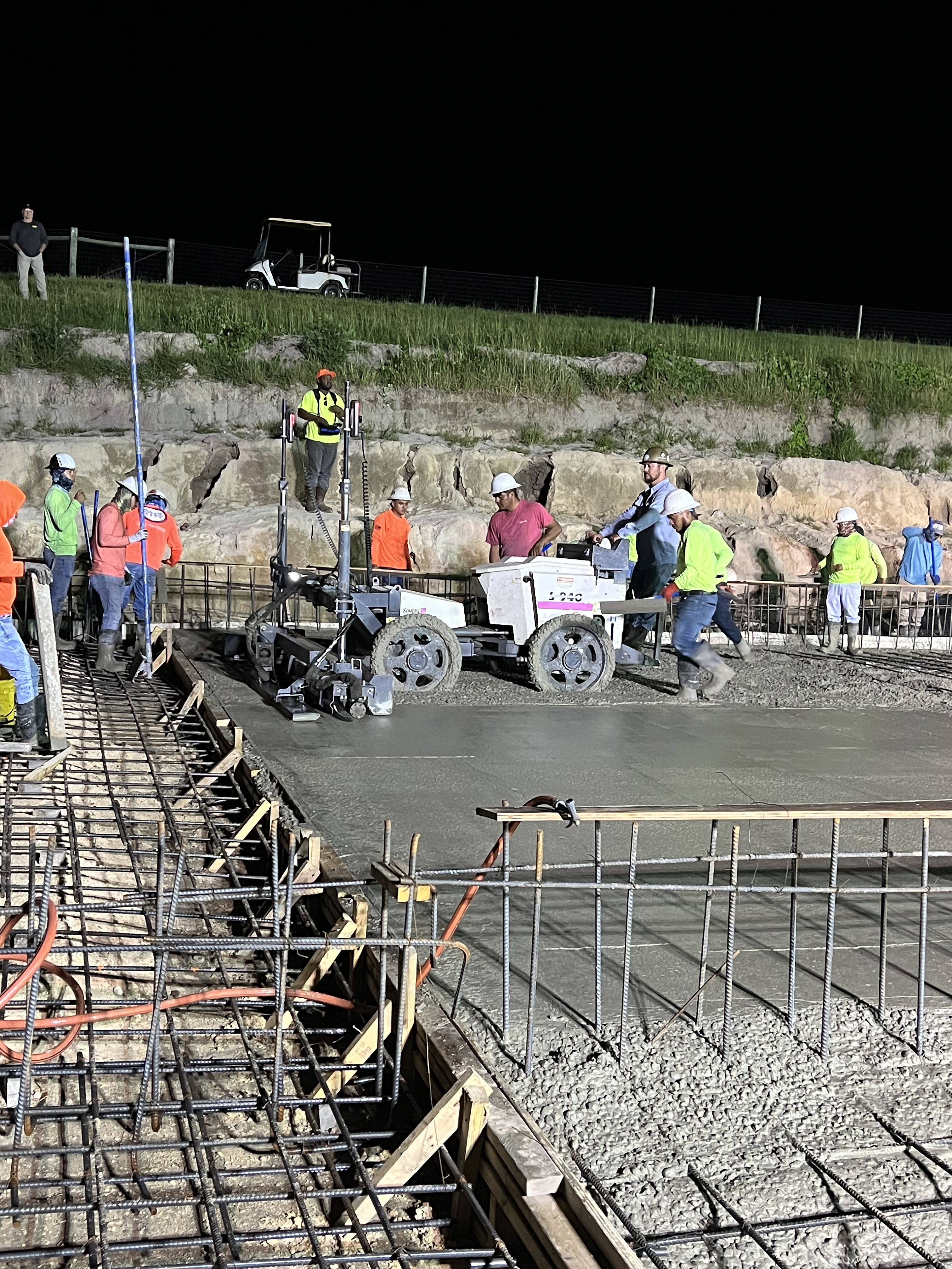 Laser screed working the wet concrete slab at night with crew alongside