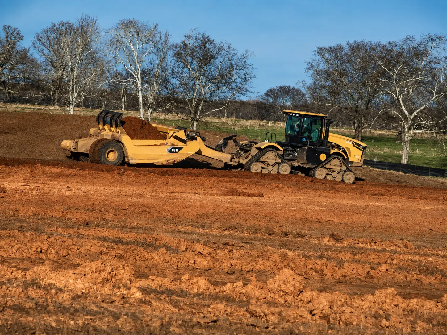 Pan scraper moving clay across a cut-and-fill site