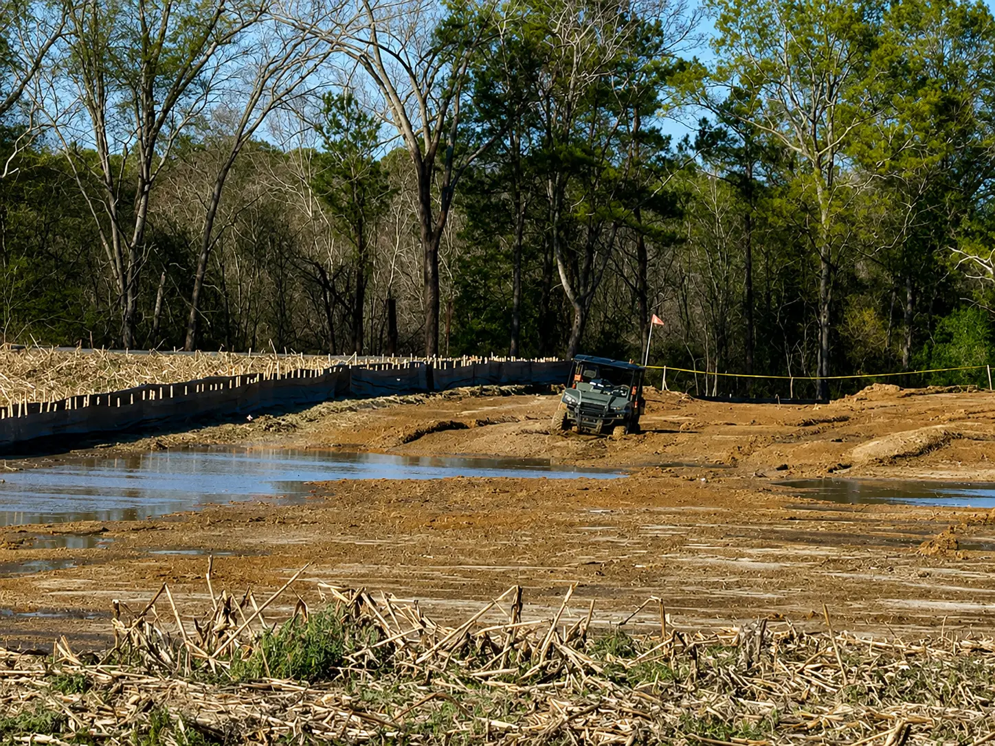 UTV parked on muddy ground beside an installed silt fence run