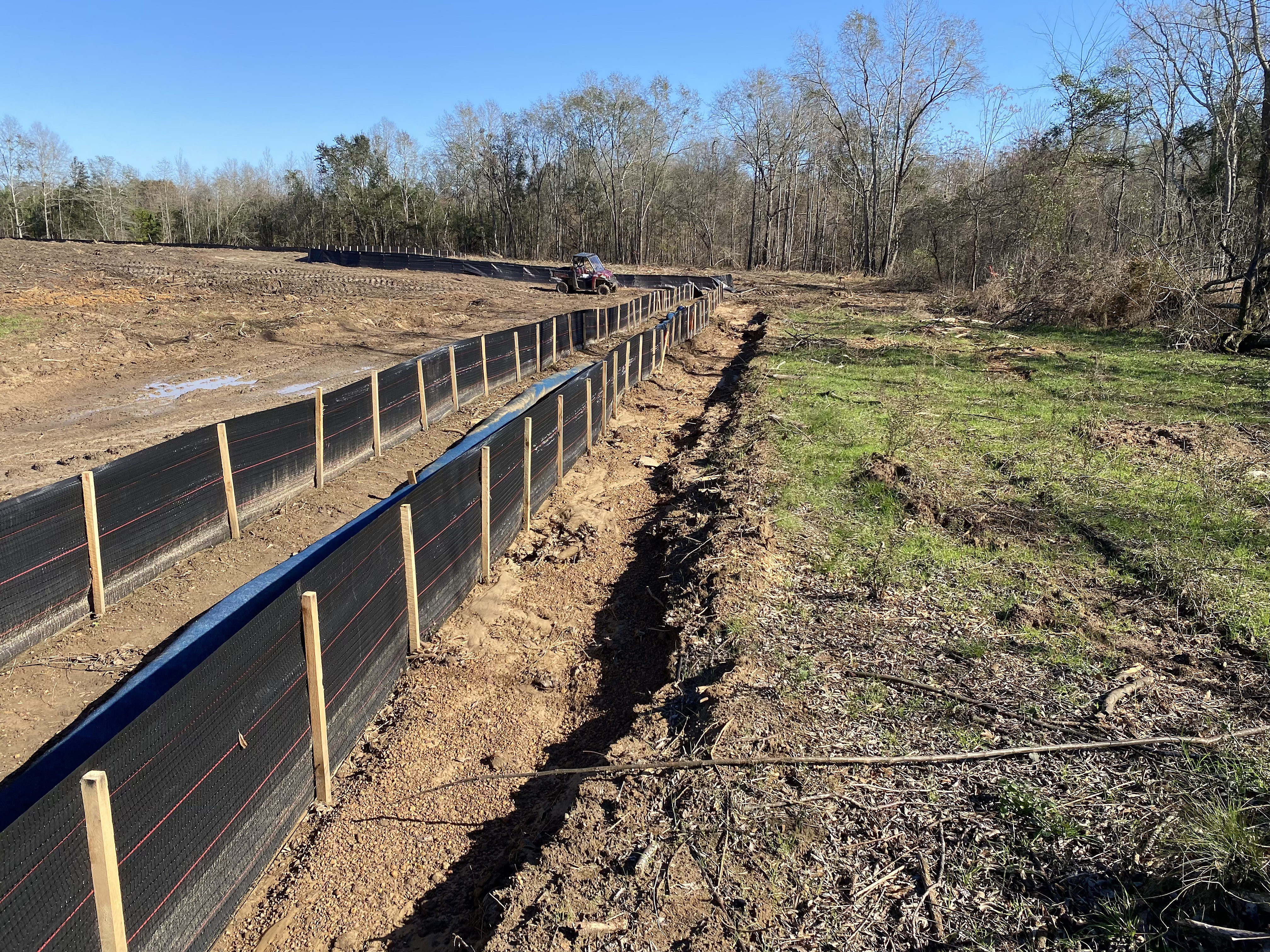 Two parallel silt fences running along cleared ground